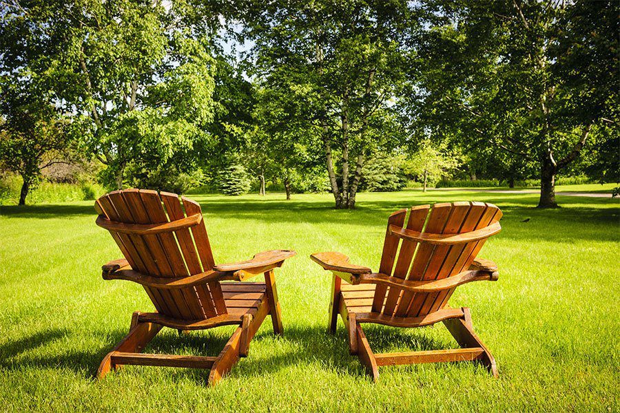 two adirondack chairs in a well moved field in summer 