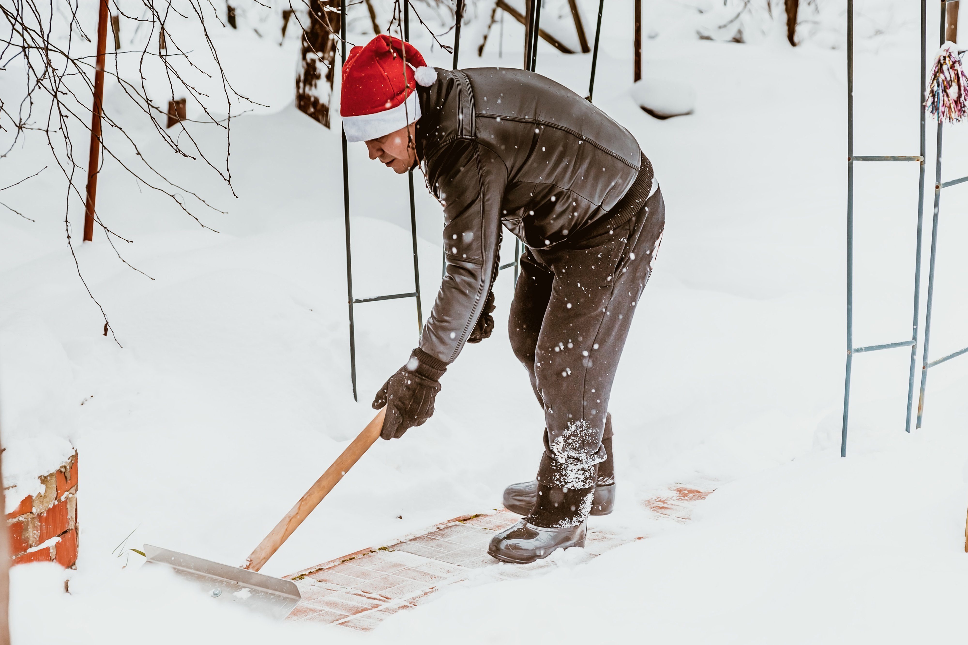 Man with santa hat shoveling path to his house 